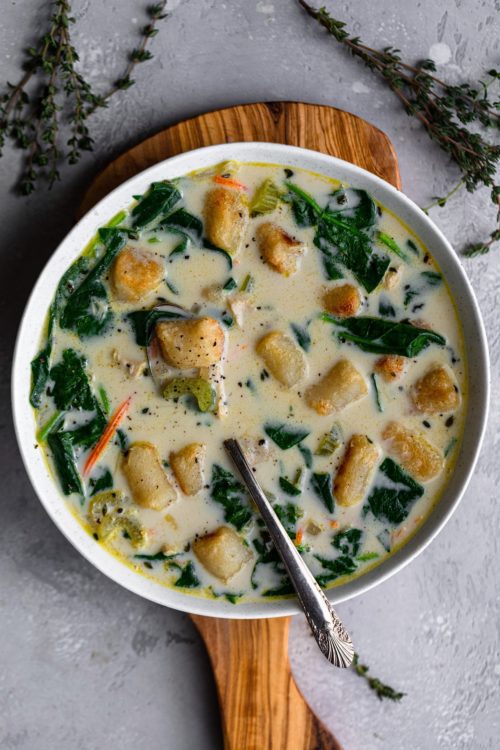 Large bowl filled with creamy chicken and gnocchi soup with chunks of chicken, fresh spinach, carrots and celery.