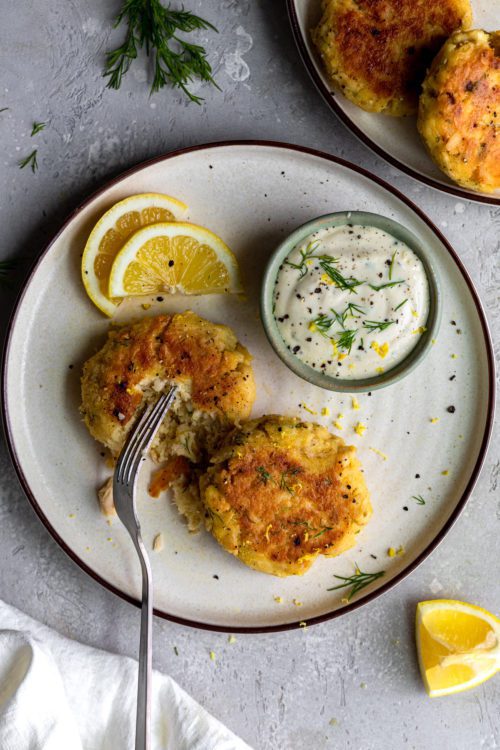 Lemon Dill Tuna Cakes being cut in half with a fork on a white plate.