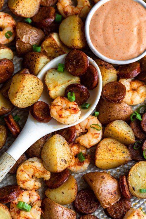 Close up of shrimp, sausage and potato Cajun sheet pan meal with a white pot of comeback sauce.