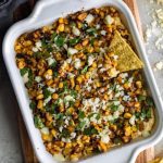 Mexican Street Corn Dip pictured from above in a white baking dish with corn tortilla chips and fresh lime wedges scattered around.