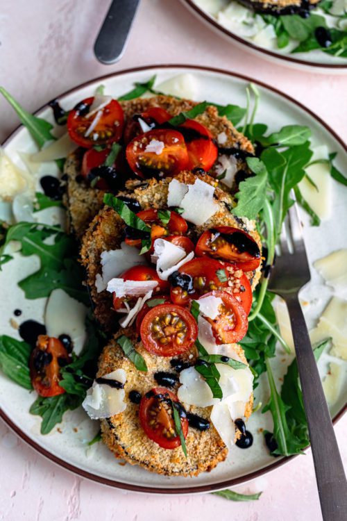 Air Fryer Eggplant Milanese on a plate with cherry tomatoes, arugula, parmesan shavings and a balsamic glaze.