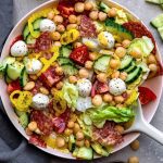 Overhead shot of an Italian salad in a pink bowl loaded with salmon, tomatoes, mozzarella balls, cucumbers and chickpeas.