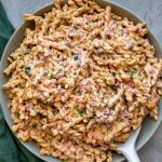 Bowl of pimento pasta salad on a grey background with a spoon in it ready for serving.
