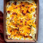 Bacon Cheddar Ranch Mashed Potatoes topped with melted cheese and bacon bits in a brown serving dish on a grey stone background.
