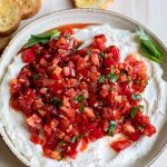 Whipped ricotta bruschetta dip with crostini on a light wood background.