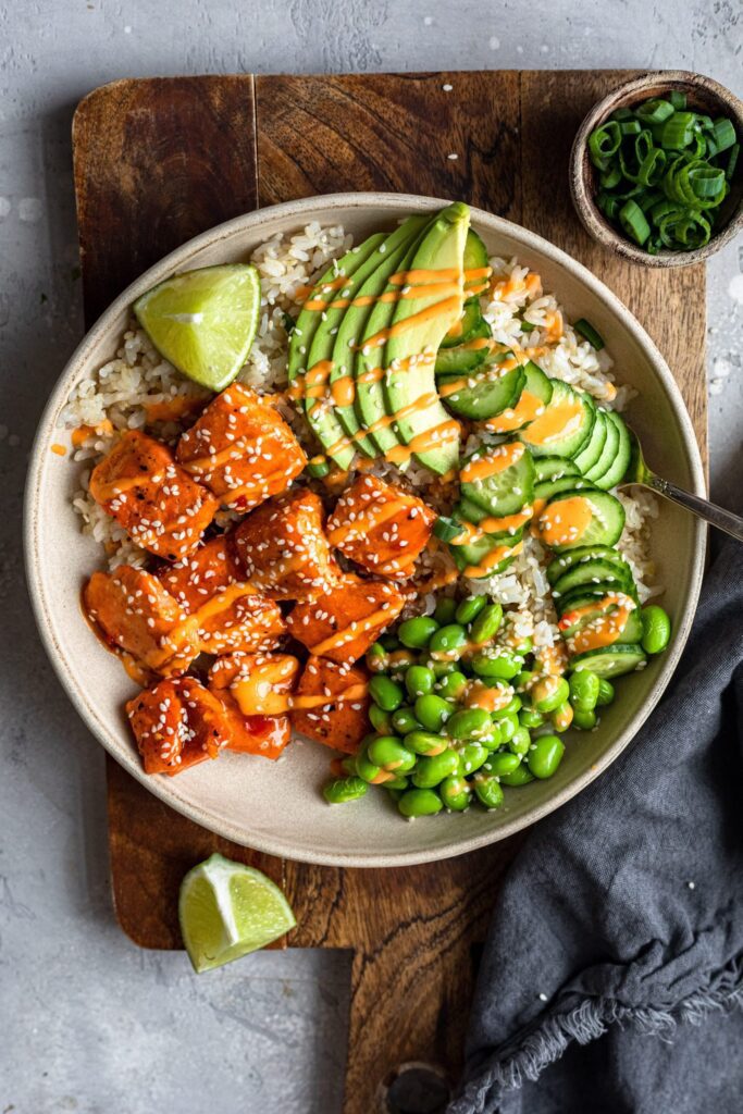Rice bowl with salmon, avocado, edamame, cucumbers, spicy mayonnaise and fresh lime garnish.