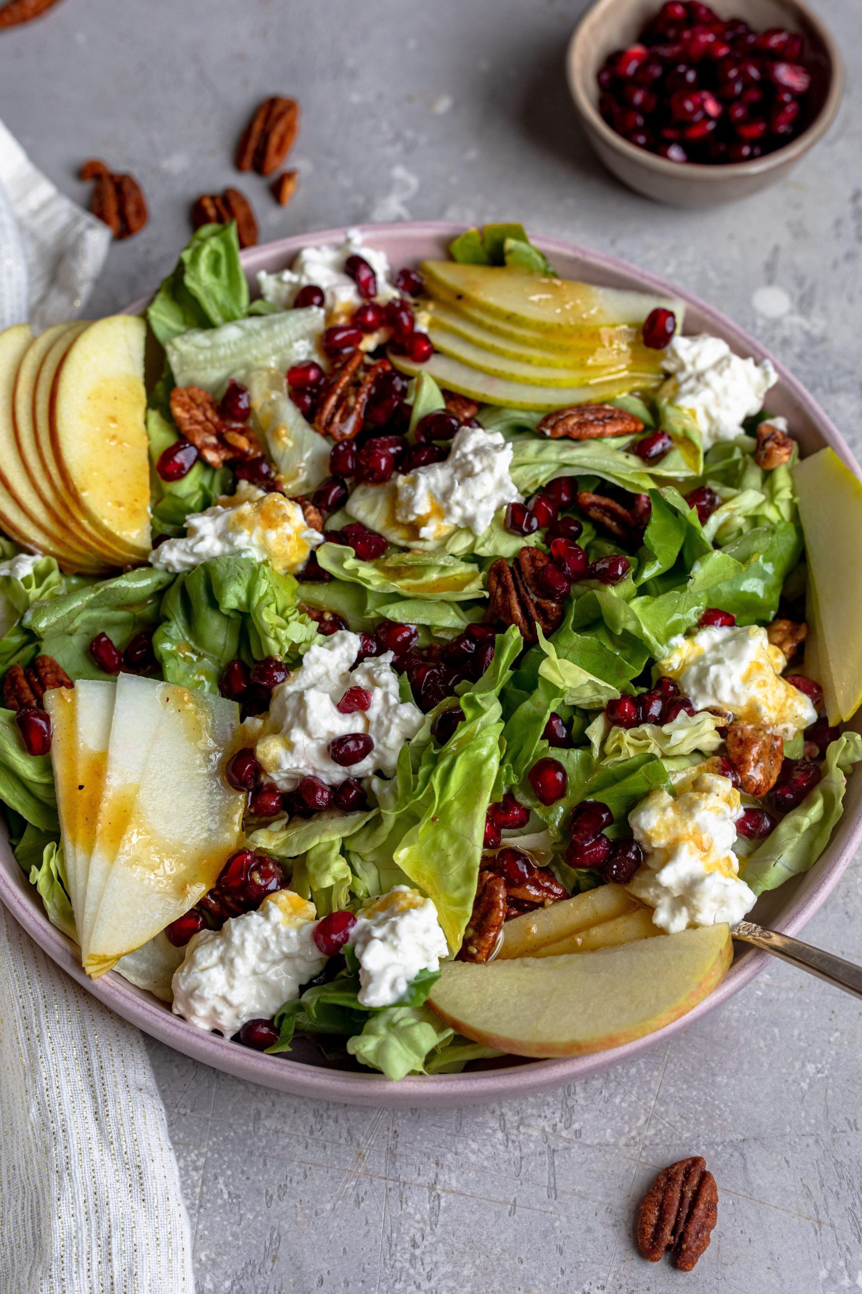 A large salad bowl filled with fresh lettuce, burrata, apple, pear, pomegranate and candied pecans.