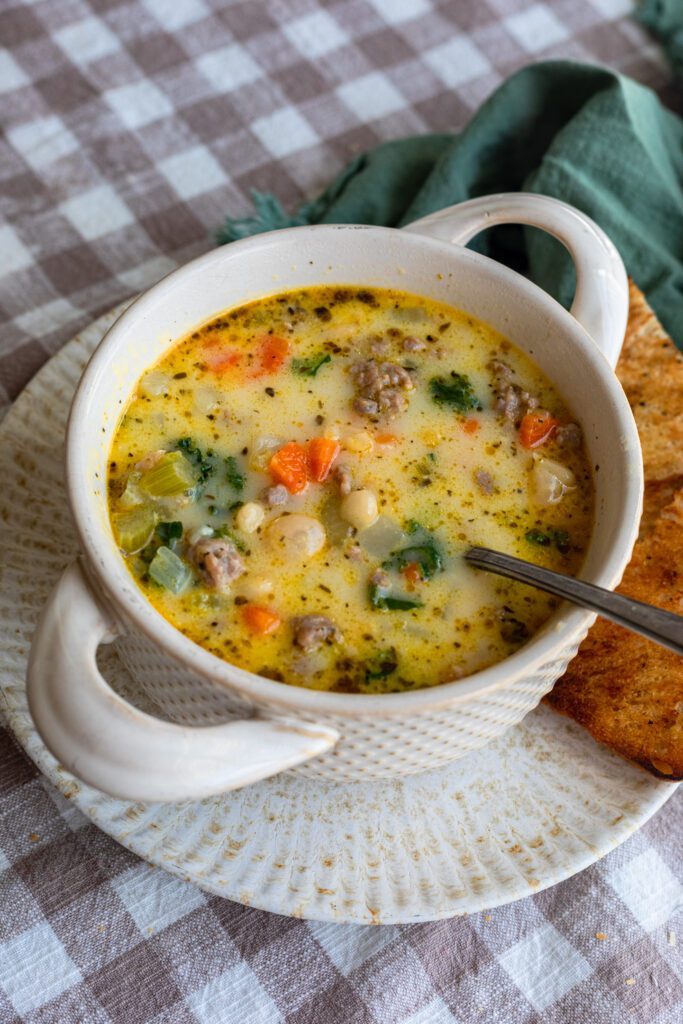 A hearty bowl of Tuscan Sausage Soup packed with veggies and tender meat, accompanied by crispy bread for dipping in.