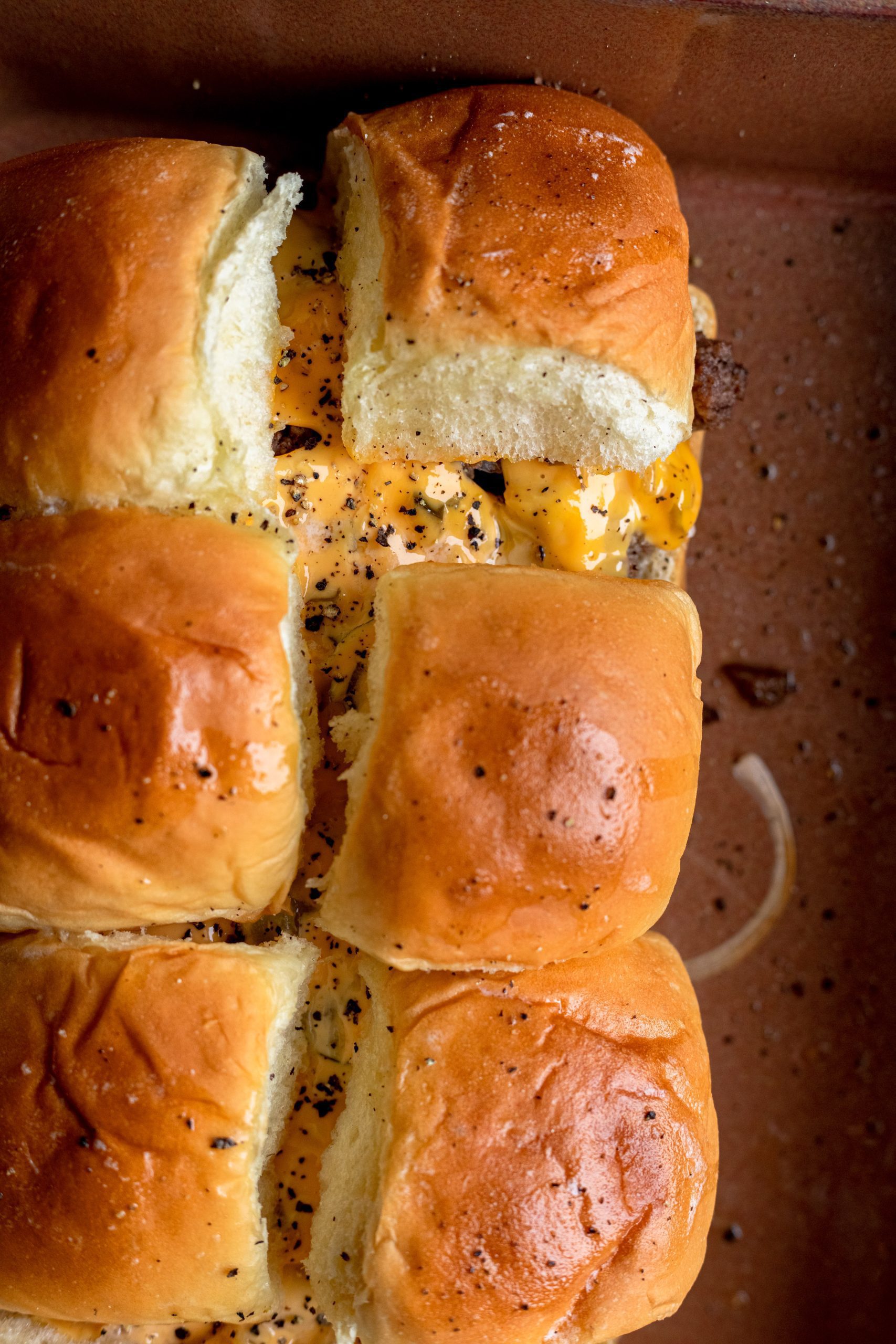 Overhead shot of a pan full of freshly baked cheeseburger sliders with melted cheese and generous seasoning.