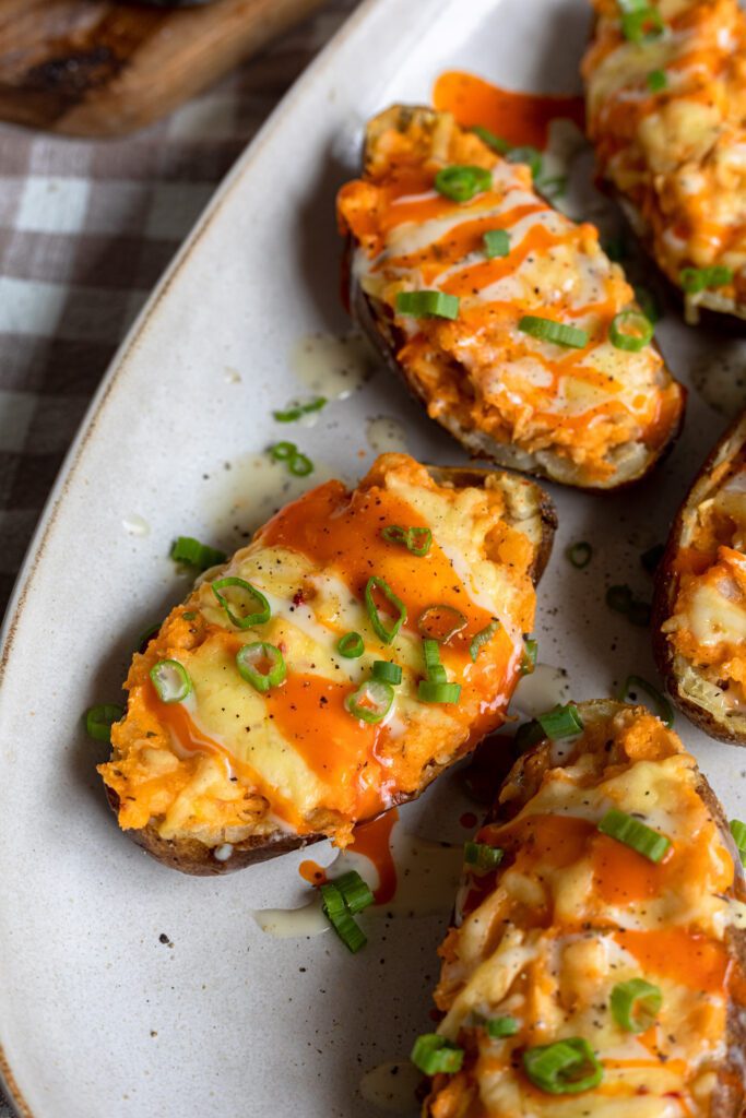 Close up shot of hot Buffalo Chicken Twice Baked Potatoes with vibrant buffalo filling, melted cheese, ranch dressing and chopped green onion. 