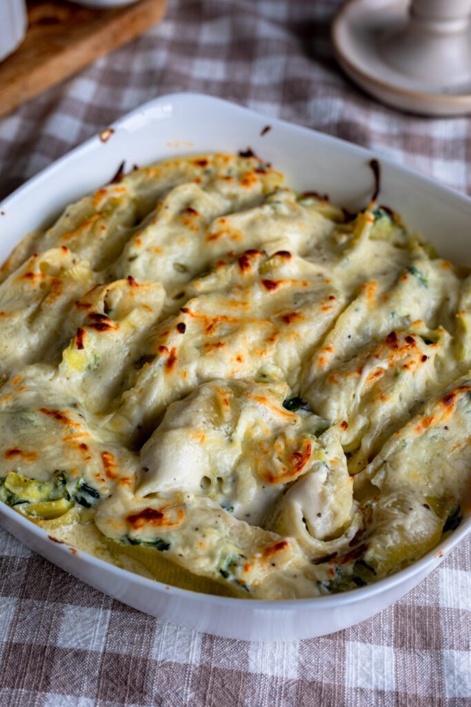 A white oven dish filled with spinach and artichoke stuffed shells, topped with golden baked mozzarella cheese.