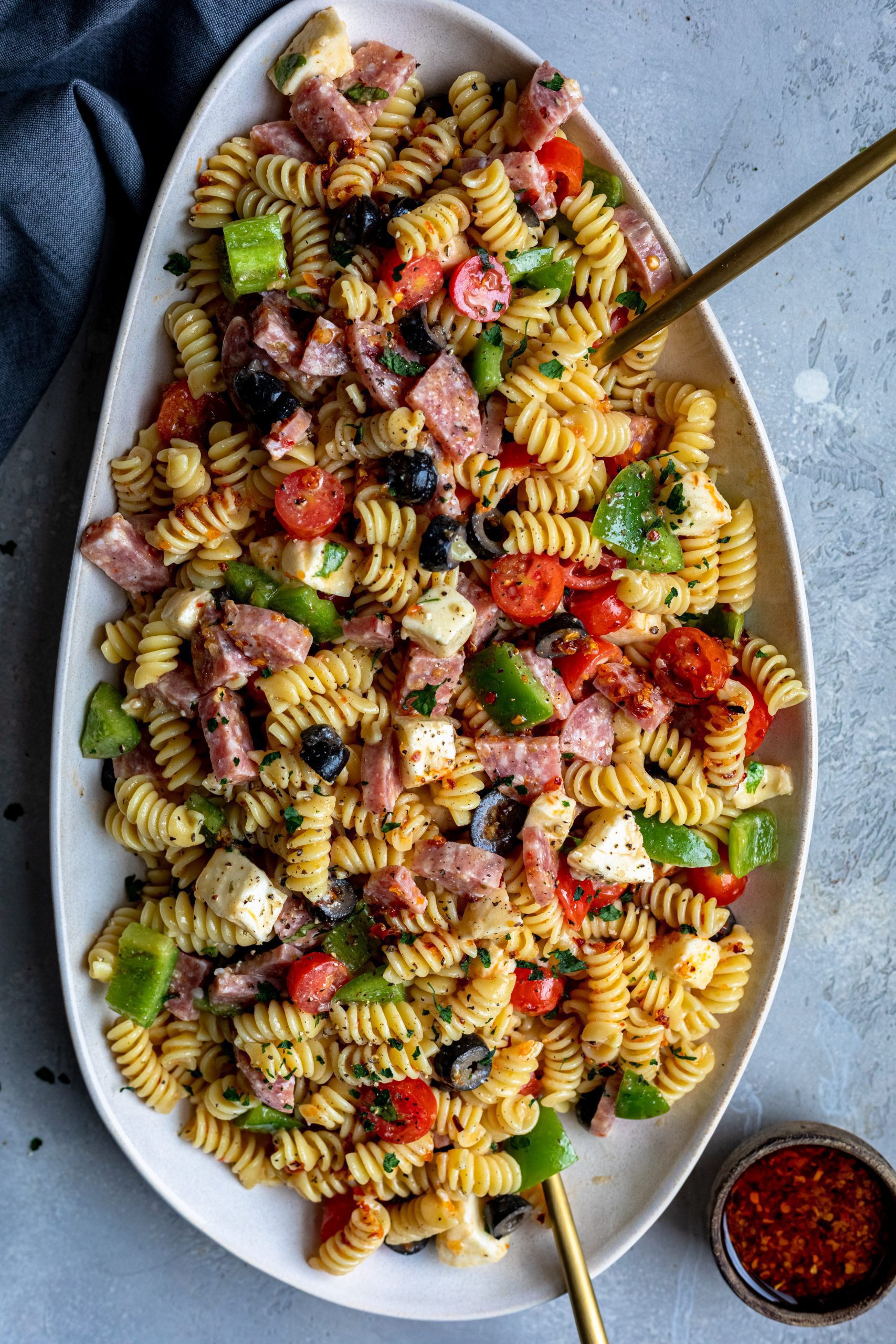 A heaping dish of italian pasta salad, loaded with various cooked meats and fresh vegetables.