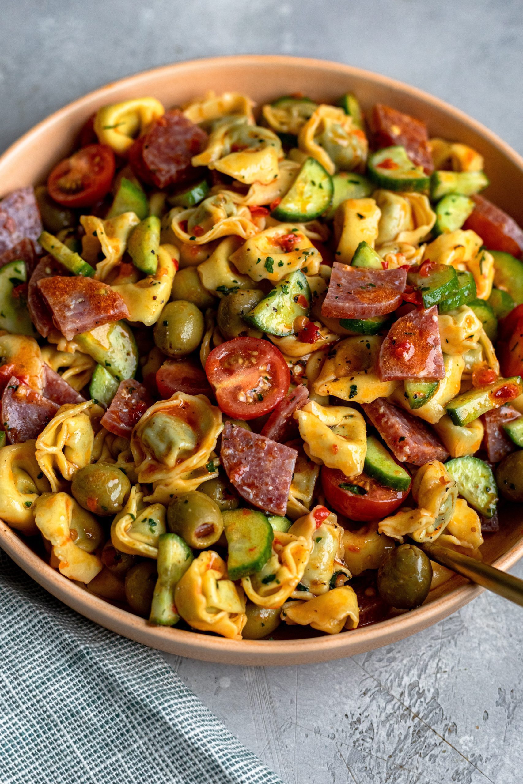 A heaping serving bowl of spicy tortellini salad with fresh vegetables, salami and pepperoni pieces. 