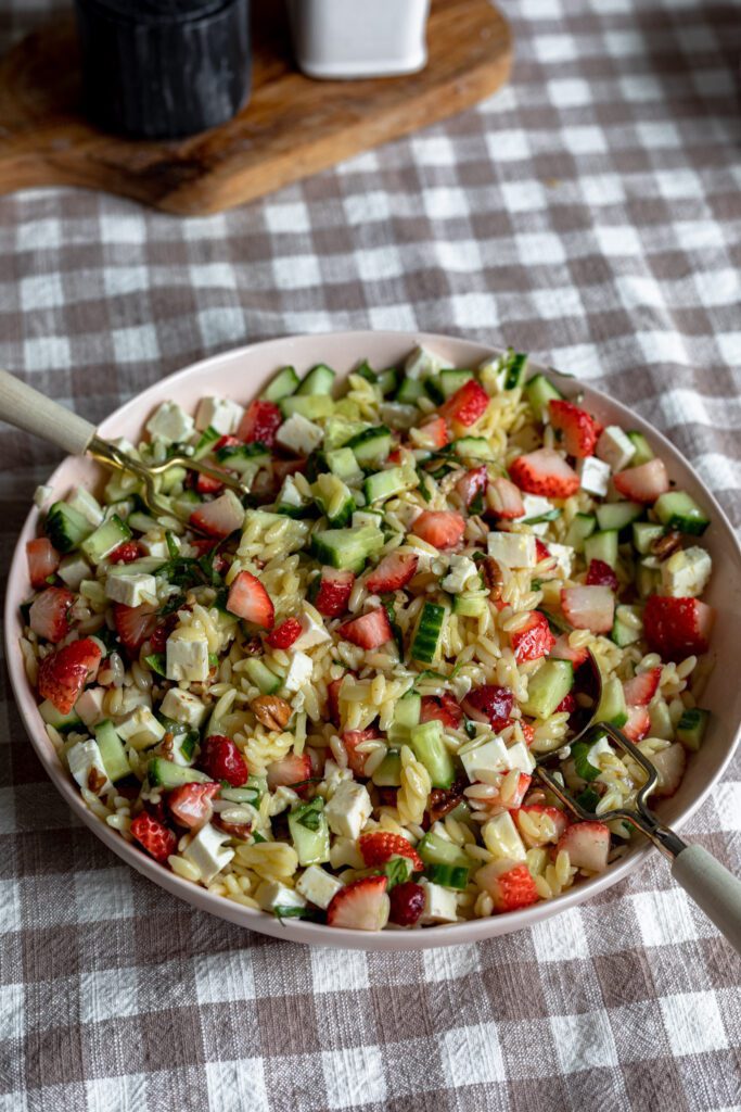 A heaping bowl filled with a strawberry basil feta orzo pasta salad with fresh vegetables and champagne vinaigrette.